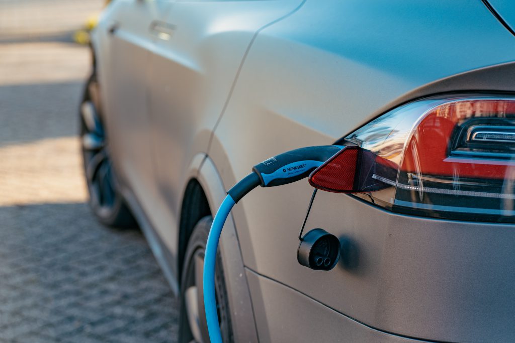 EV home charging cable plugged in to back left red light of a matte silver  car on a driveway.