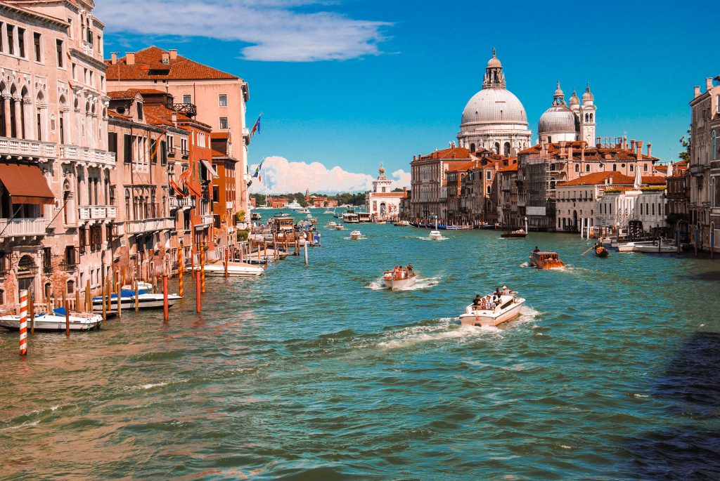 picturesque image of a canal in Venice with small boats, and buildings either side of the canal
