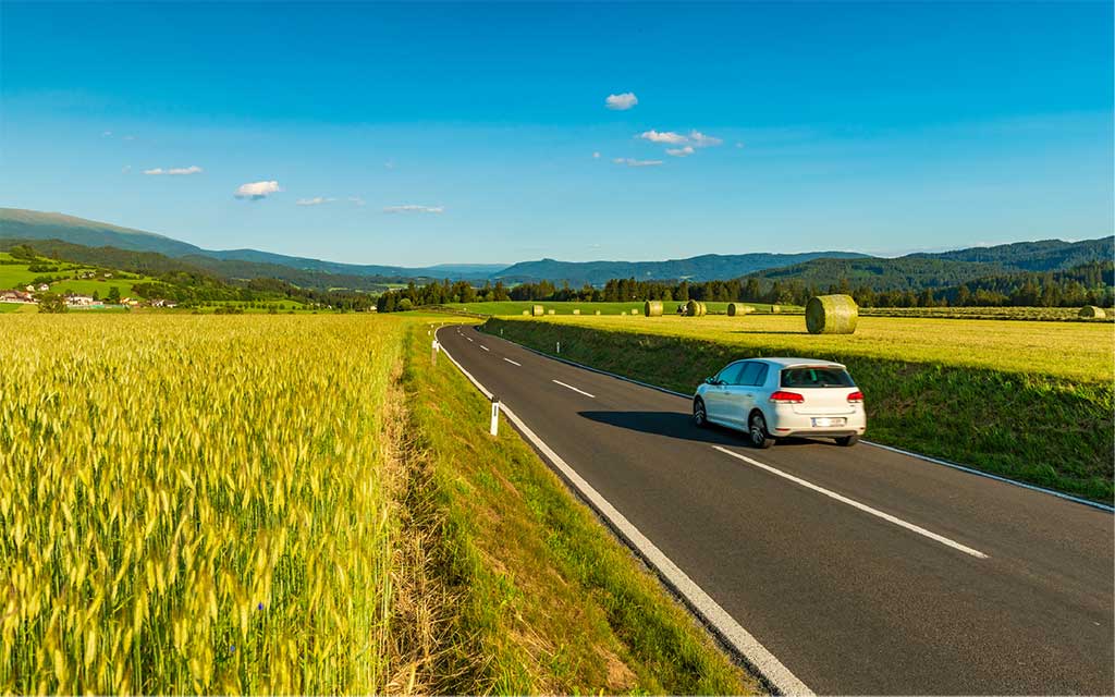 A white car is driving through the European countryside.