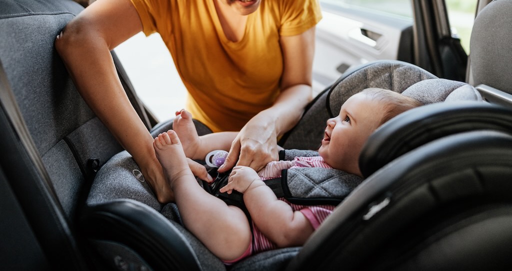 A baby is being secured in a rear-facing car seat.