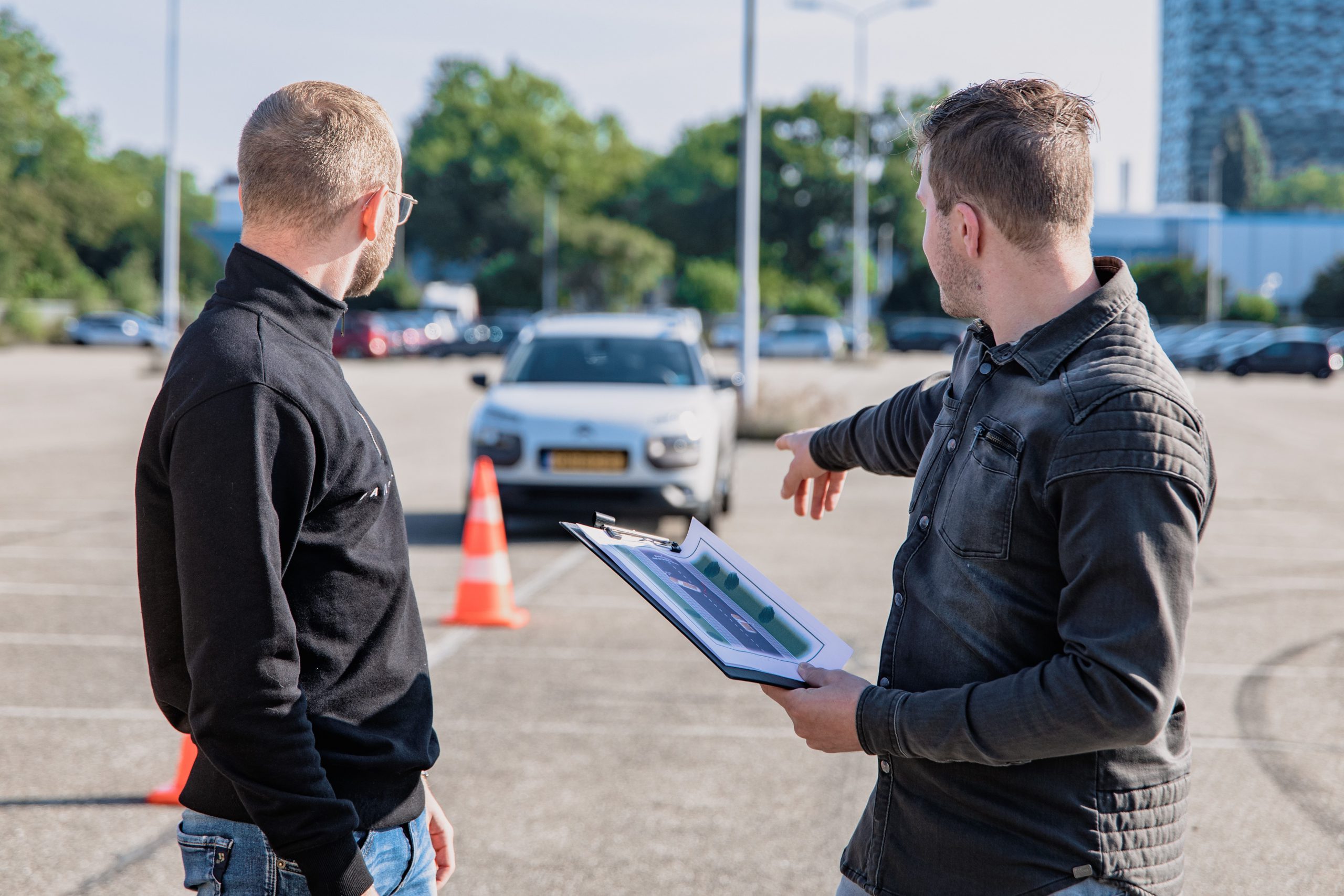 two people pointing towards a car with a clipboard showing a manoeuvre