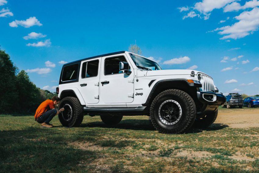 person fixing back right tyre of Jeep outside on grass