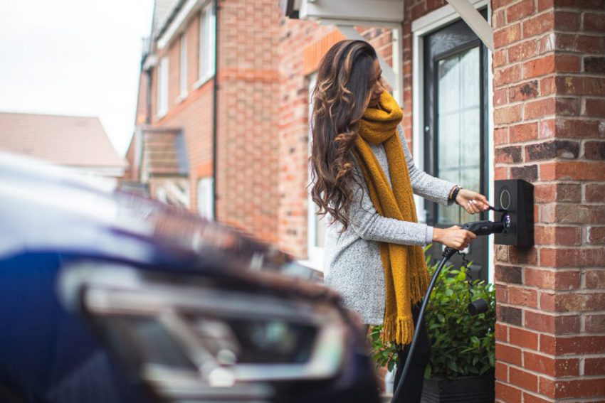 person with long brown hair plugging EV charger into wall unit
