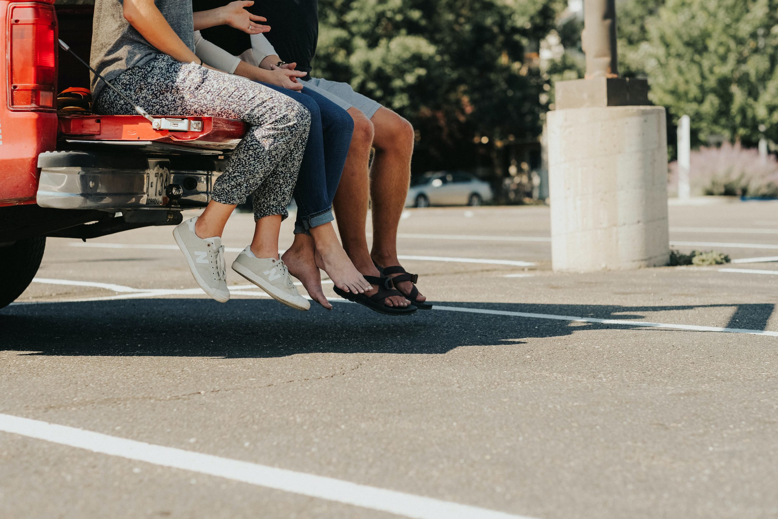 three people sat on the edge of a vehicle's boot in an empty car park, with only their torsos-down visible.