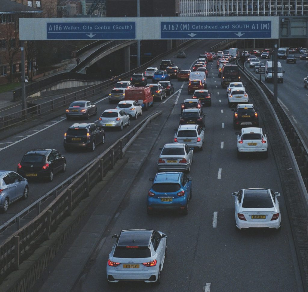 Cars of different ages, makes, and models driving on a busy road.