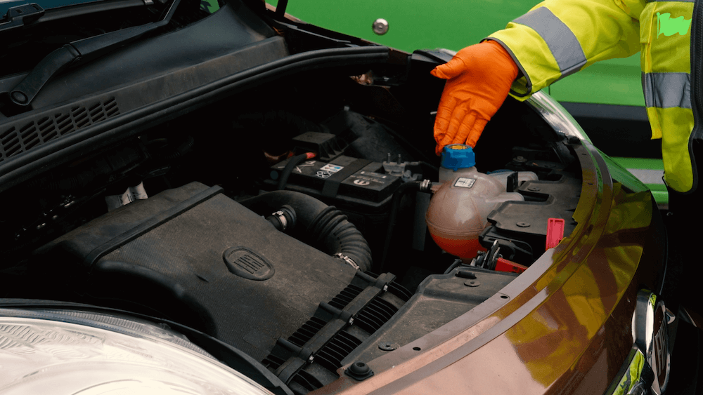 A Green Flag technician points to the coolant reservoir under the hood of a car.