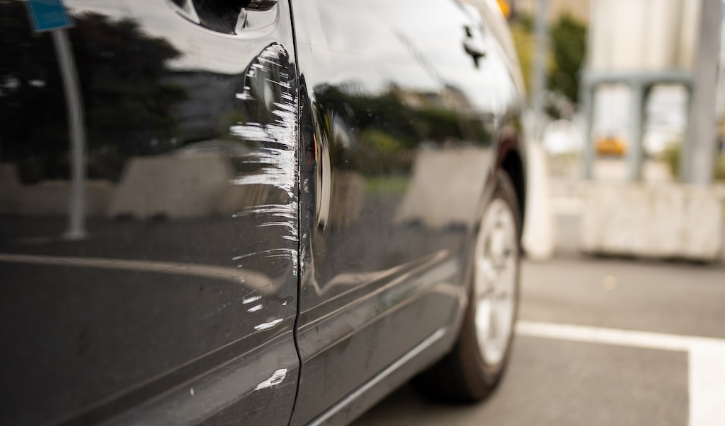 A black car with a small dent and scratches is parked.